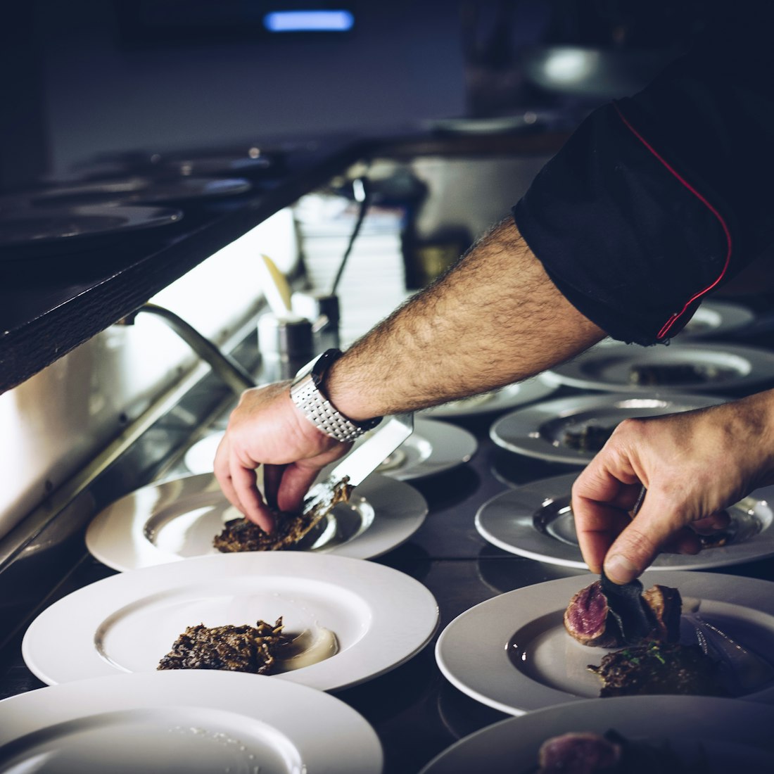 Hands plating at the pass in a dark kitchen